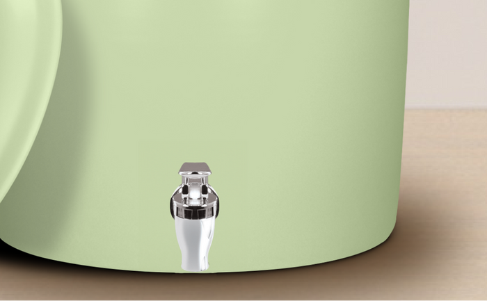 Close-up of a light green water dispenser with a shiny silver and white spigot, placed on a wooden surface.