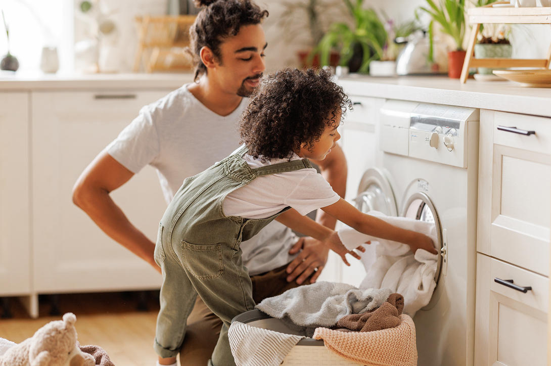 Father and child loading laundry into a washing machine in a bright home, representing clean, high-quality water throughout the home with Brio whole house filtration systems.