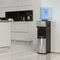 A Stainless Top Load Water Cooler - 520 Series with a blue water jug stands against the wall in a sleek, minimalist kitchen featuring light cabinets and a tiled floor.