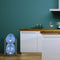 A modern kitchen with white cabinets, a wooden countertop, the gray Single Column 2-Bottle Storage Rack holding two large blue water jugs, glass jars, a blender, and a wine glass on the counter against a teal wall.