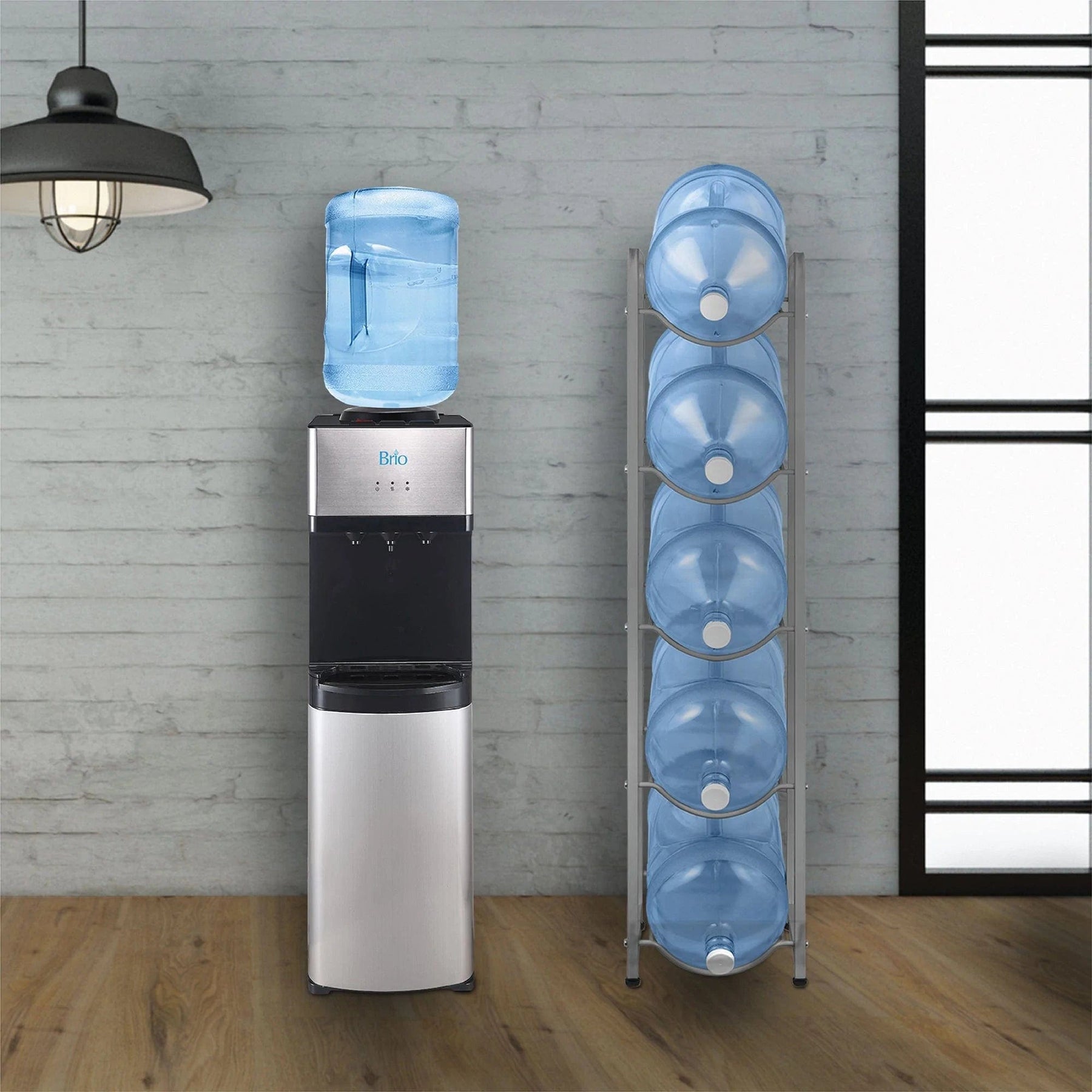 A water cooler stands next to a Brio Single Column 5-Bottle Storage Rack - Gray, which neatly holds four extra 5-gallon bottles, set against a gray wall with wooden floors and a hanging light fixture.