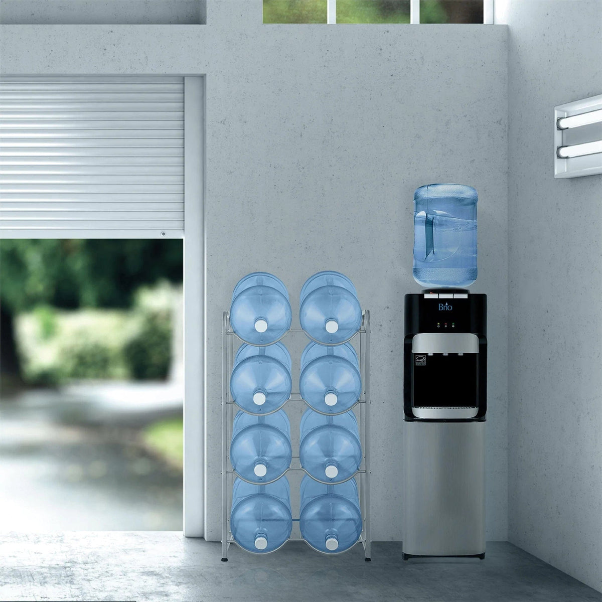A modern water dispenser with a full bottle stands beside a Double Column 8-Bottle Storage Rack - Gray, which holds eight large empty blue bottles in a bright, minimal room with a partially open garage door.